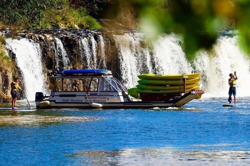 A boat with kayaks, a waterfall, and people paddleboarding. 3