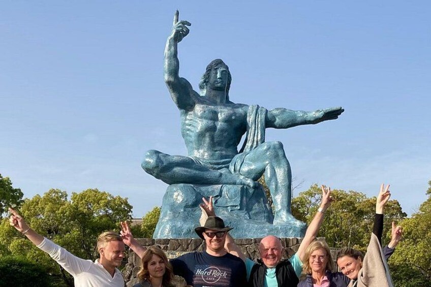 A large bronze statue of a seated figure with arms raised, surrounded by greenery and a clear sky. 3