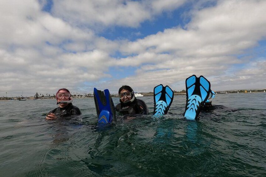Three people in water with fins, a boat in the background, and a cloudy sky. 3