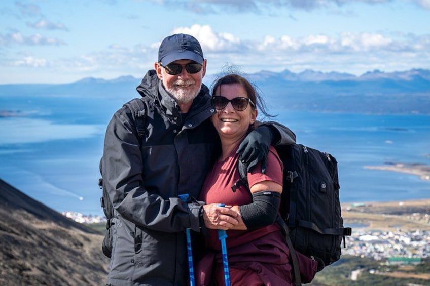 Two people hiking with backpacks, overlooking a mountainous landscape and a body of water. 1