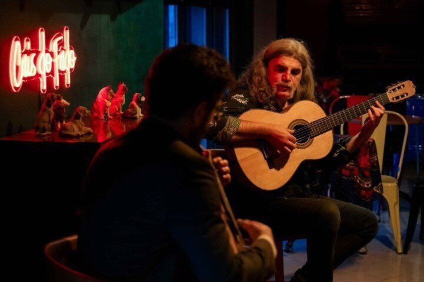 En person spiller akustisk guitar på en scene, med et neon-skilt i baggrunden. 3