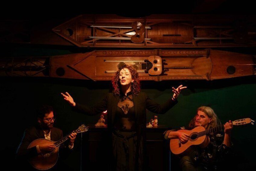 En person med armene udstrakte i et svagt oplyst rum med træmøbler og en guitarist i baggrunden. 5