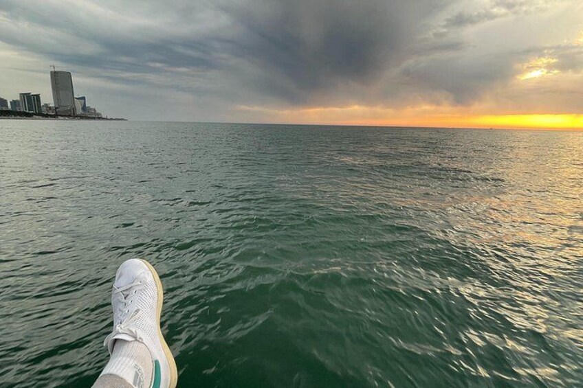 A person's foot in a white sneaker on a boat, with a city skyline and a sunset in the background. 4