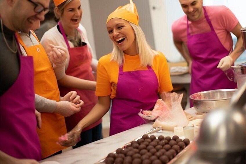 Un groupe de personnes portant des tabliers, dont certaines ont un chapeau, se trouve dans une cuisine. On peut voir sur le comptoir des produits enrobés de chocolat. 3