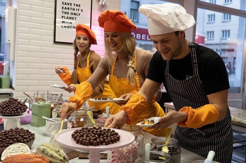 Trois personnes dans une cuisine, en train de préparer des plats, avec des décorations au chocolat et une pancarte sur l’importance de préserver la planète. 5