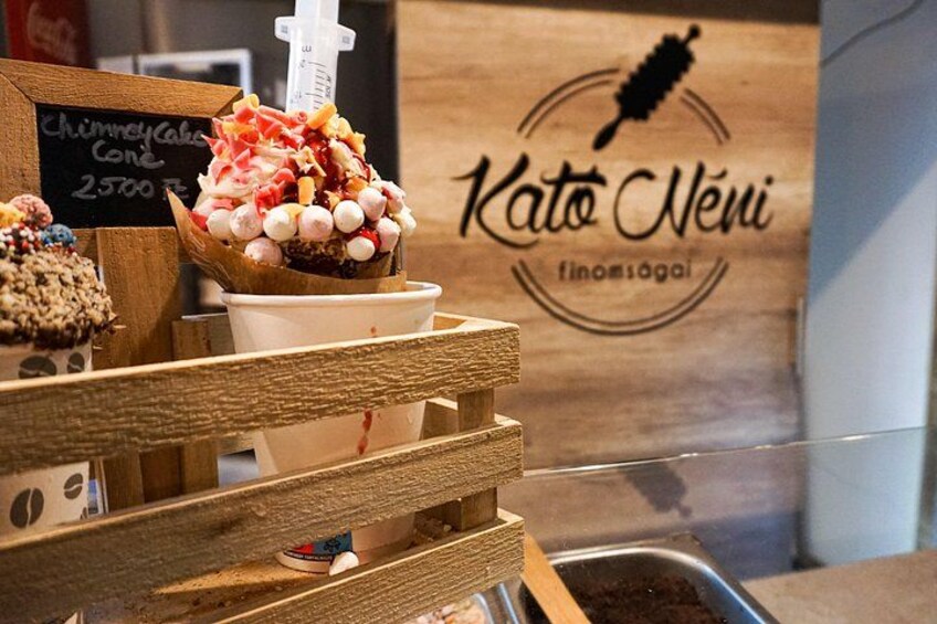 Un puesto de postres con un cartel que dice 'Kato Neni' y una barra de madera. 2