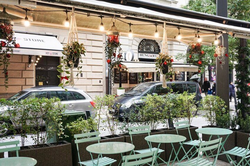 An outdoor cafe with green chairs and tables, hanging decorations, and parked cars. 4