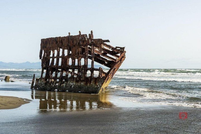 A rusted shipwreck on a beach with waves crashing against it. 5