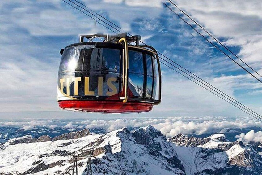 Un teleférico con la etiqueta 'TTLIS' suspendido sobre un paisaje montañoso nevado. 1