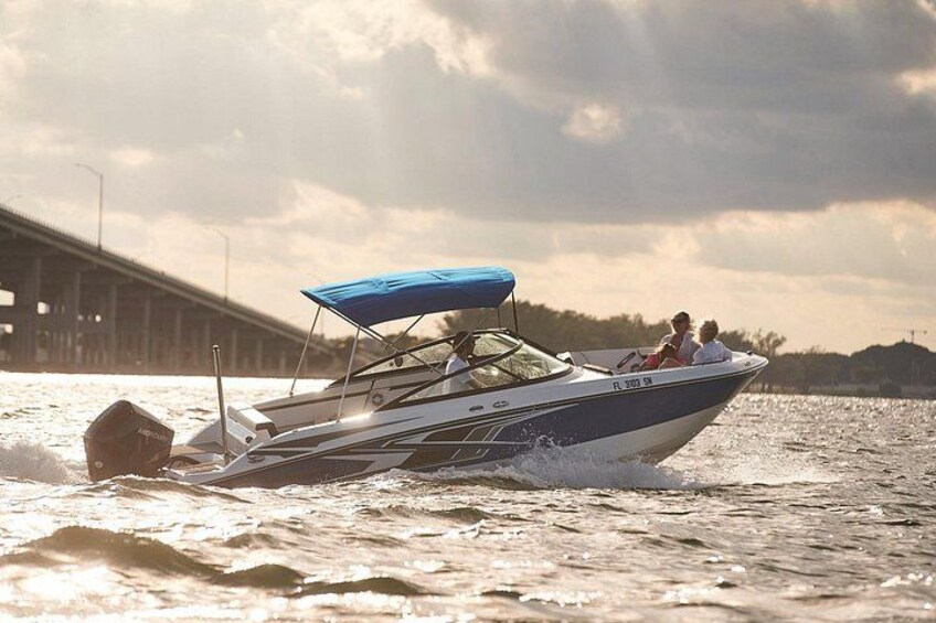 Un bateau à moteur rapide avec un auvent bleu, naviguant sur l’eau, avec un pont en arrière-plan. 3