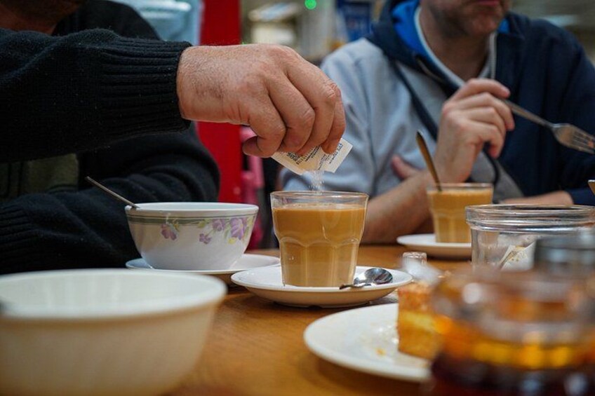 Une personne verse du thé dans une tasse, tandis que d’autres tasses et un pot sont posés sur la table. 2