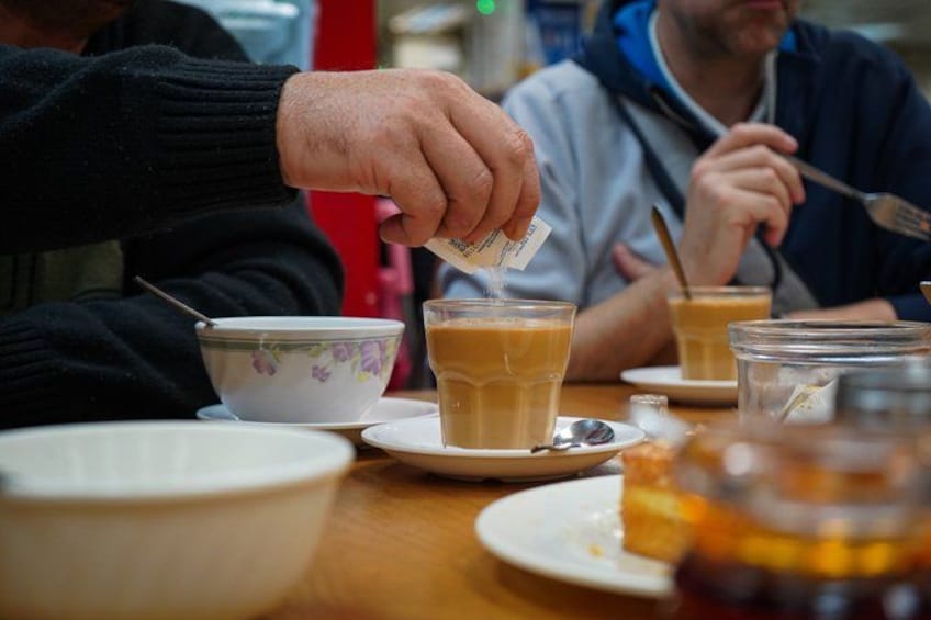 Una persona serviendo té en una taza, con otras tazas y una tetera sobre la mesa. 5