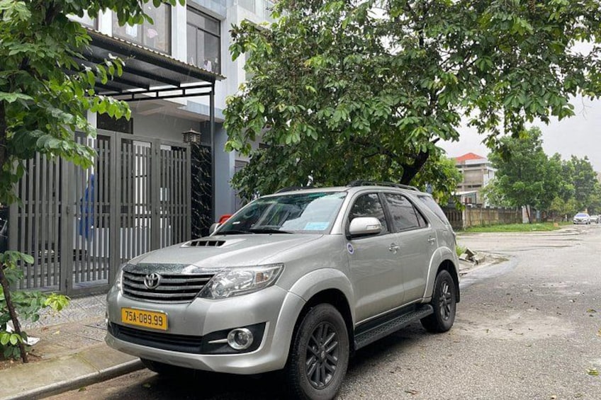 A silver Toyota SUV parked on a residential street with a gated entrance and a tree in the background. 3