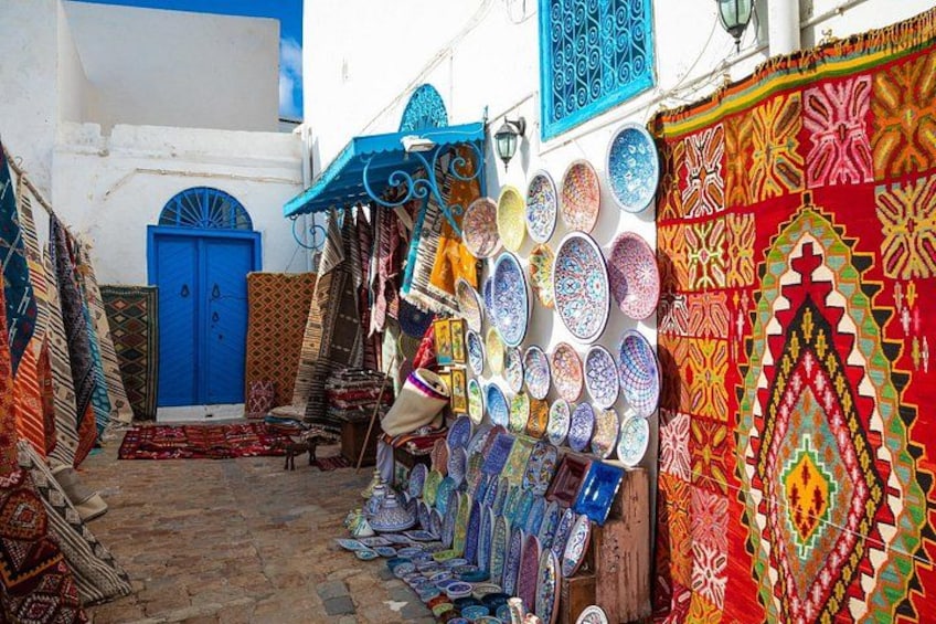 Une ruelle étroite où sont exposés, le long des murs, des textiles et des objets en céramique aux couleurs vives. 4