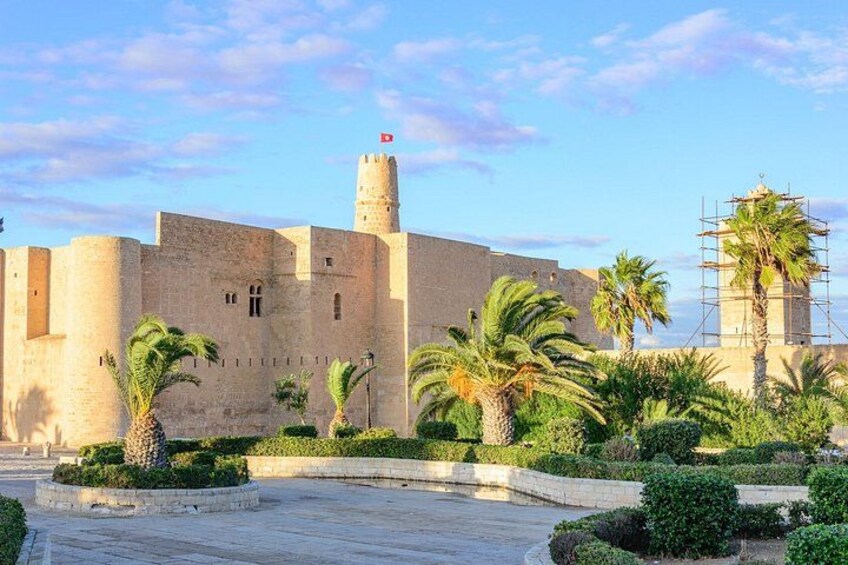 Une forteresse historique dotée d’une tour centrale, de palmiers et surplombant un ciel dégagé. 1