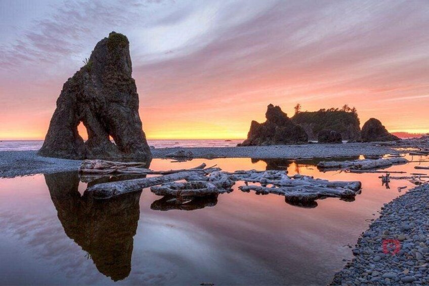 A rocky coastline with a prominent rock formation in the foreground and smaller formations in the background during sunset. 3