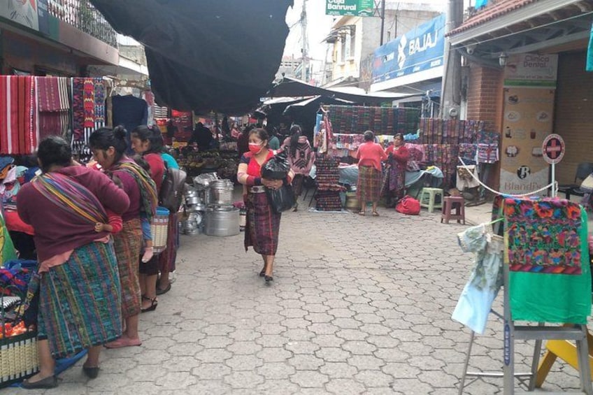 A market with vendors and customers, stalls with textiles, and a paved ground. 1