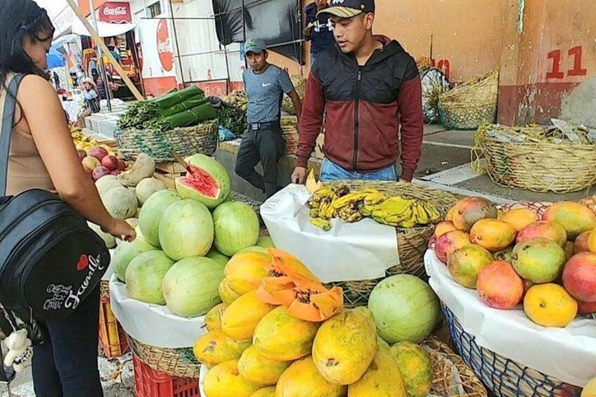 A fruit market with various fruits like watermelons, bananas, and mangoes on display. 5