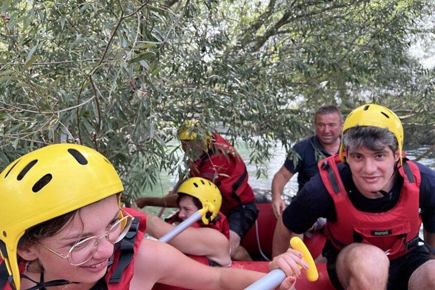Personas en una balsa, con cascos y chalecos salvavidas, remando por un río rodeado de árboles. 5