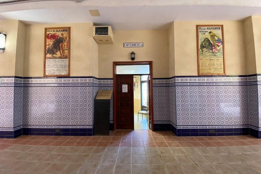 Un couloir aux carreaux décoratifs, une porte portant l’inscription « INFERRERIA », et des affiches sur les murs. 5