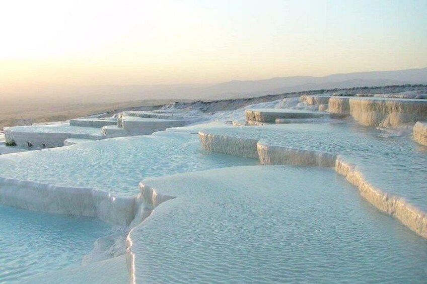 Terraced pools of clear water, likely a hot spring, with a flat horizon and distant mountains. 3