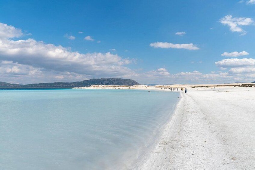A beach with clear water, a sandy shore, and distant mountains. 2