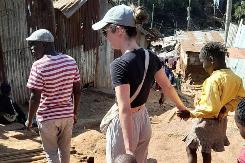 A rural setting with people standing and interacting, a corrugated metal structure, and a dirt ground. 2