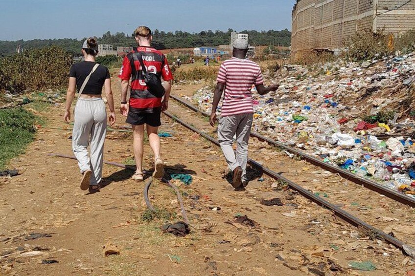 Three people walking along a railway track with trash scattered around. 2