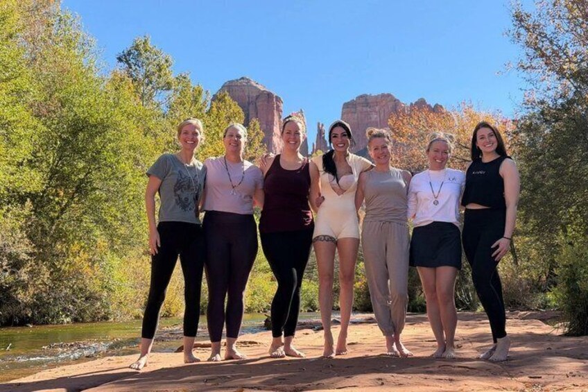 A group of people standing on a dirt path with a river and rocky formations in the background. 1