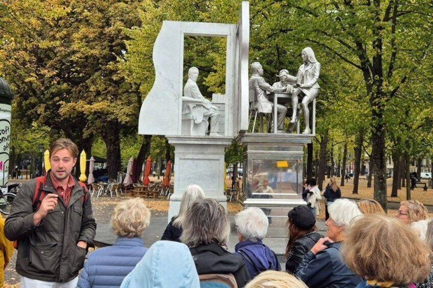 A statue of two figures in a park with trees and a crowd of people. 2