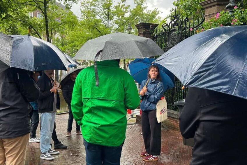 A group of people standing on a wet pavement, some holding umbrellas. 5