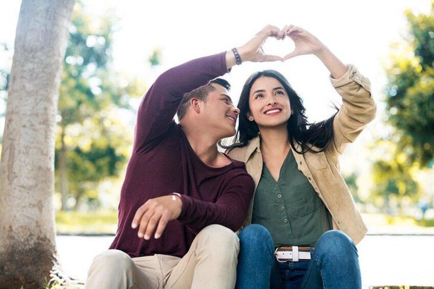 Two people sitting on a bench outdoors, one making a heart shape with their hands. 5