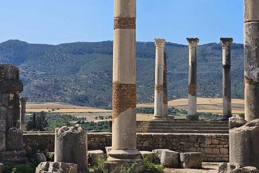 Ancient ruins with columns, a stone staircase, and a mountainous landscape in the background. 1