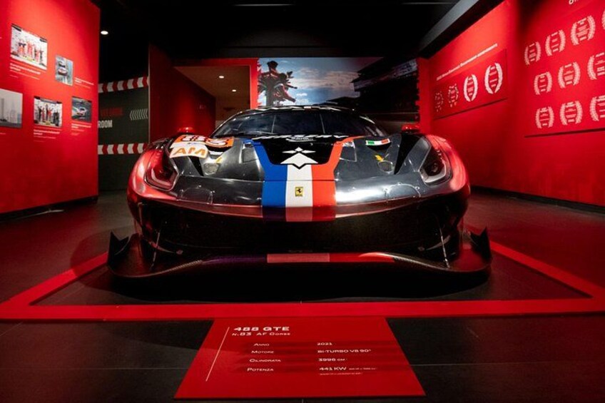 Un coche deportivo exhibido con una franja roja y azul, rodeado de paredes rojas y un suelo rojo. 3