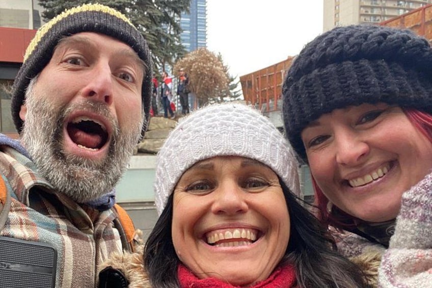 Tres personas tomándose un selfie al aire libre, con edificios y árboles de fondo. 4