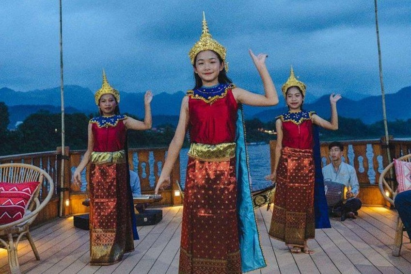 Drei Personen in traditioneller Kleidung treten auf einem hölzernen Deck direkt am Wasser auf. 3
