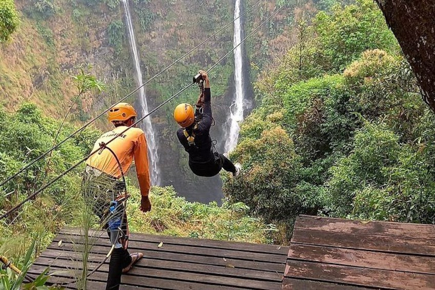 Eine Person zipline über bewaldetes Gebiet, im Hintergrund ein Wasserfall. 2