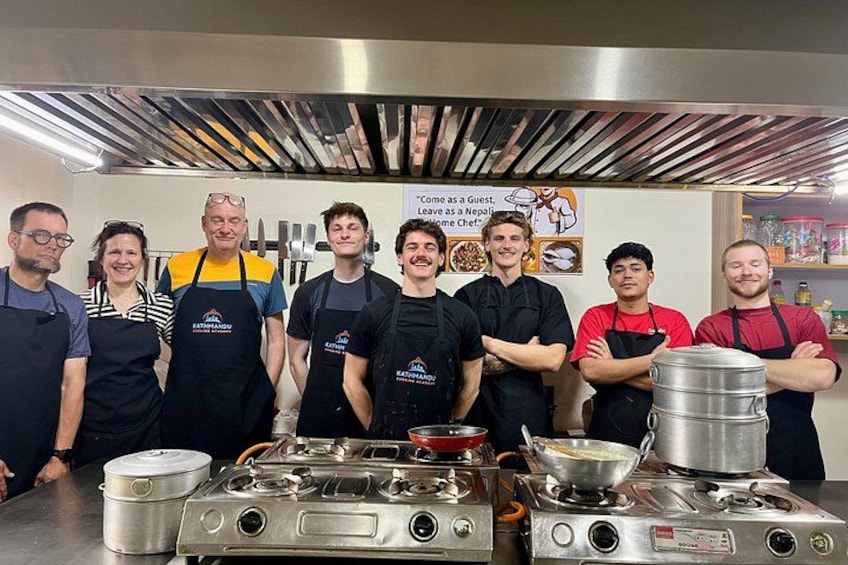 A group of people in aprons standing in a kitchen with cooking equipment. 4