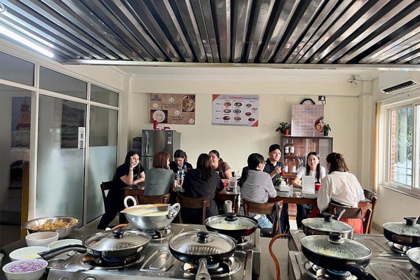 A group of people in a kitchen setting with cooking equipment and a menu on the wall. 5