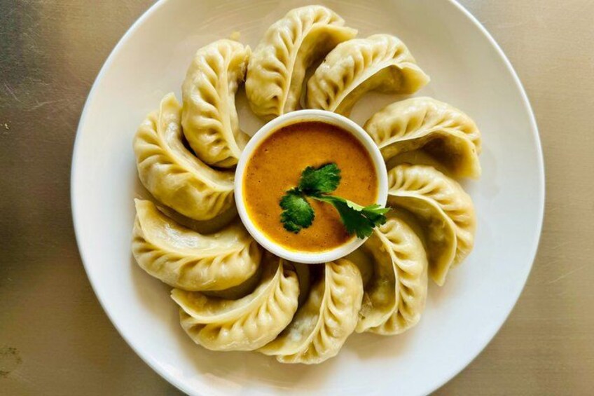 A plate of dumplings arranged in a circular pattern with a bowl of sauce in the center. 4