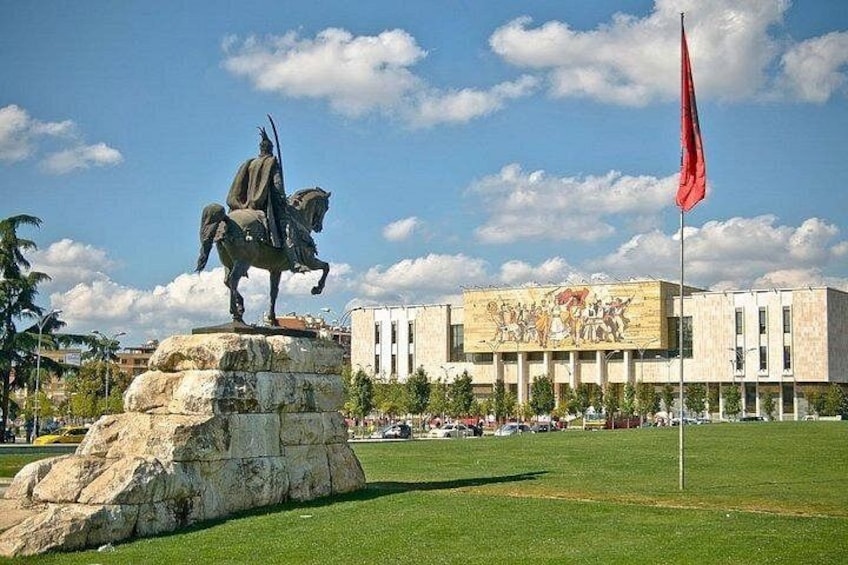 A statue on a pedestal, a building with a mural, and a flag. 1