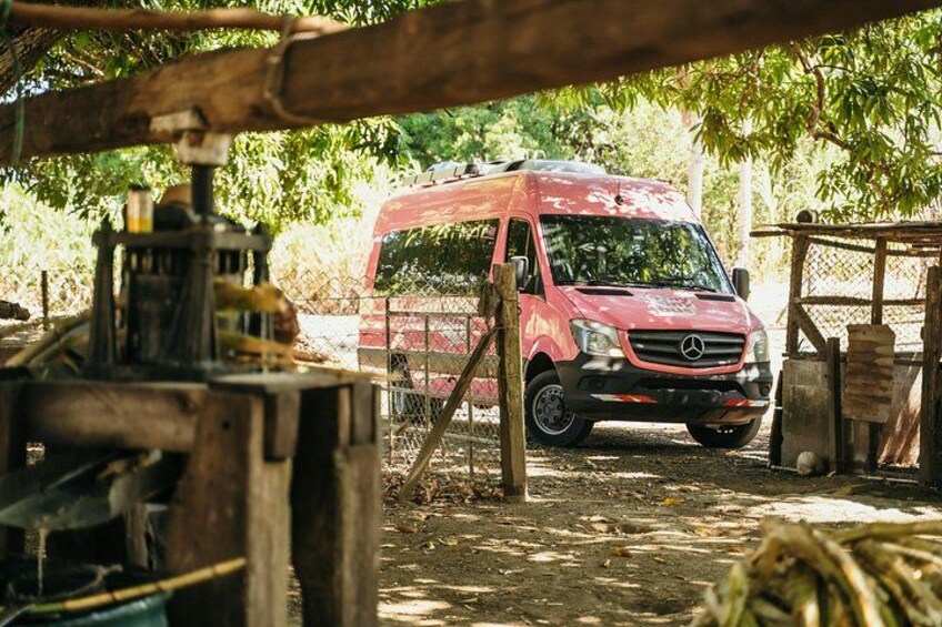 A red Mercedes van parked in a rustic outdoor setting with wooden structures and trees in the background. 5