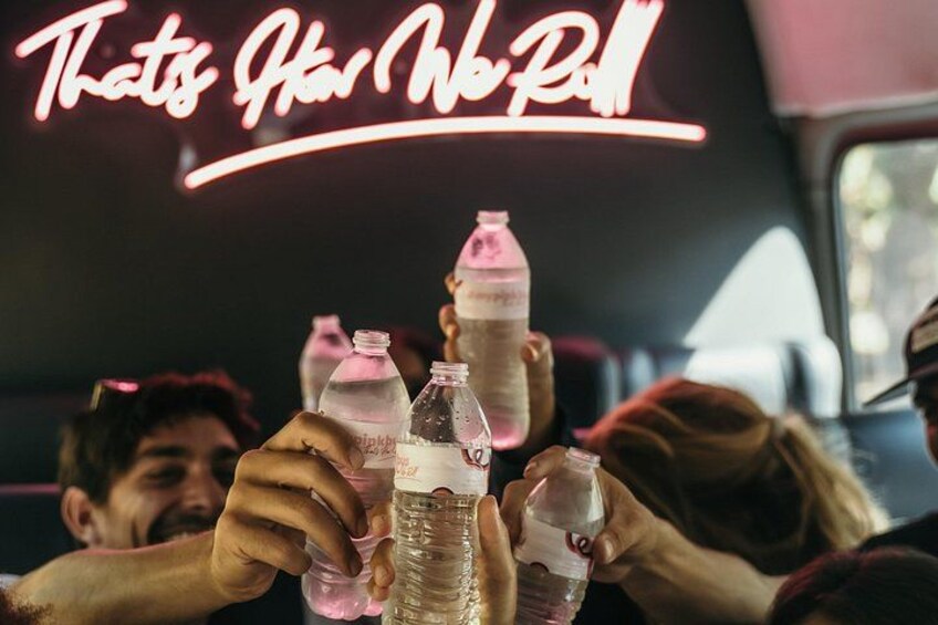 People toasting with plastic bottles in a vehicle with a neon sign reading 'That's How We Roll'. 2