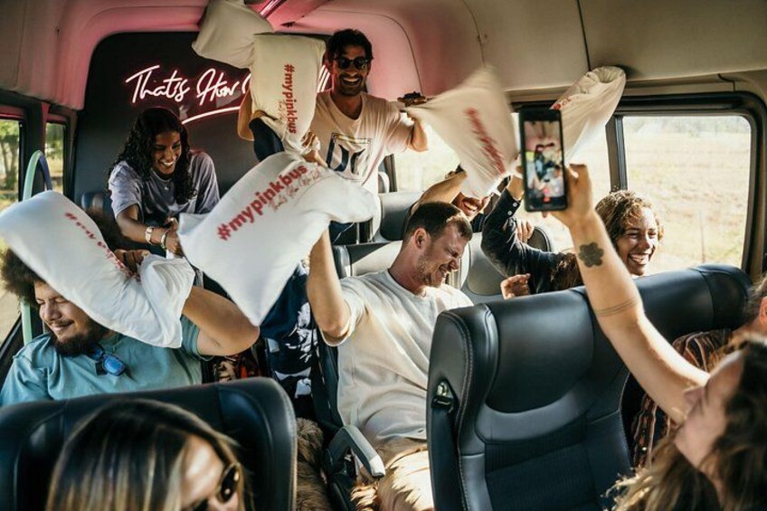 People in a vehicle, some holding white bags with red text, and a neon sign in the background. 3