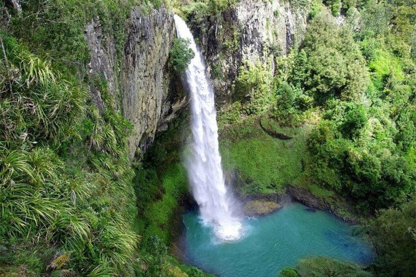 A waterfall cascading into a turquoise pool surrounded by lush greenery. 1