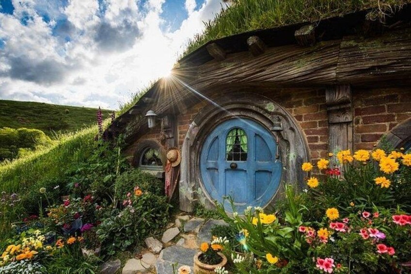 A Hobbiton-style house with a blue door, surrounded by colorful flowers and greenery. 5