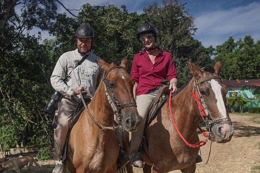 Dos personas a caballo en un entorno al aire libre con árboles y un sendero de tierra. 1