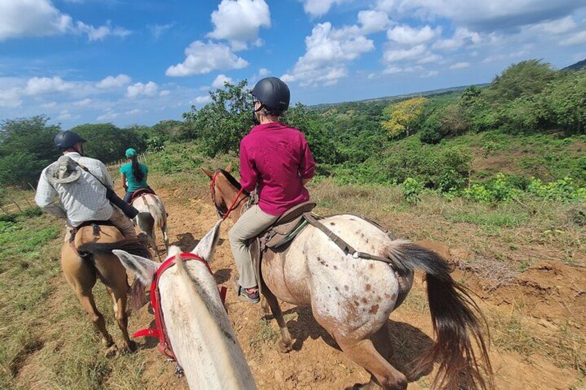 Tres personas cabalgando a caballo por un sendero de tierra en un paisaje montañoso con vegetación. 4