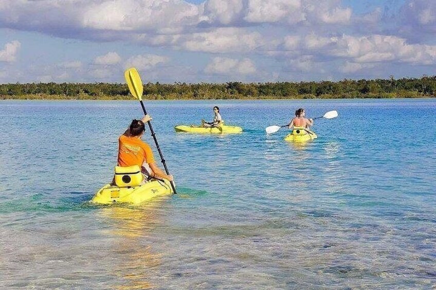Tres personas en kayak sobre aguas tranquilas, con cielo despejado y una orilla distante. 2