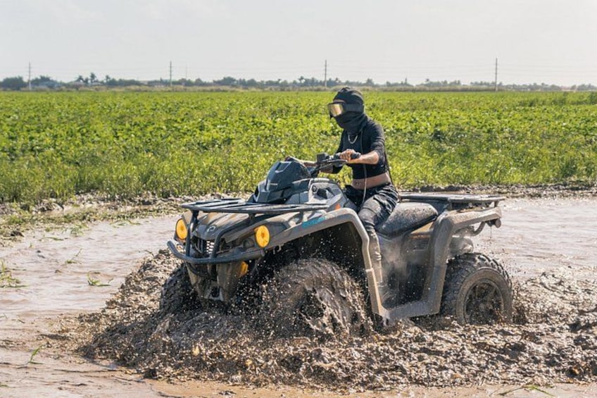 A person riding an ATV through a muddy field. 1